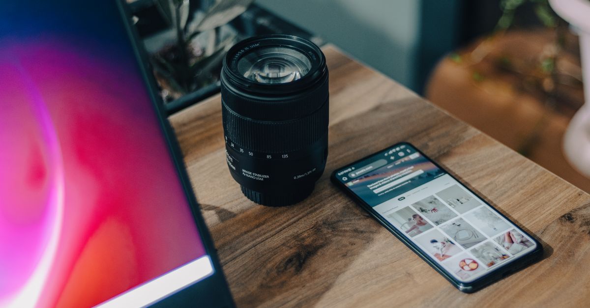 A camera lens beside a smartphone on a wooden desk, showcasing modern technology.